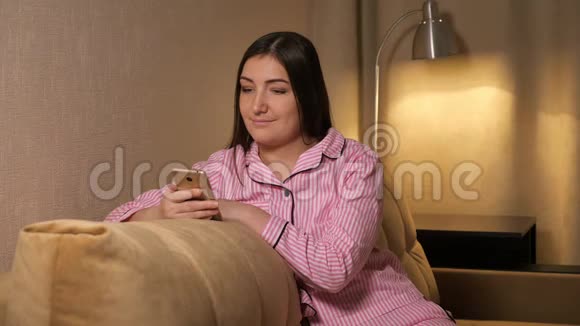 晚上的女孩坐在沙发上看着电话视频的预览图