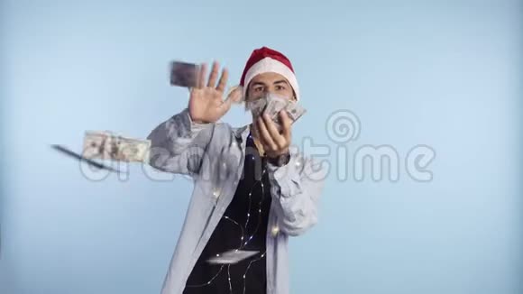 疯狂英俊兴奋的男人扔美元钞票和微笑挥霍财富戴着圣诞老人红帽子的男人视频的预览图