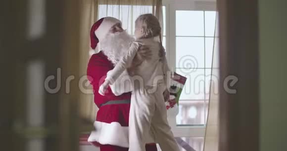穿着圣诞老人服装的白种人把漂亮的金发白种人孩子穿着睡衣扎着辫子的微笑女孩视频的预览图