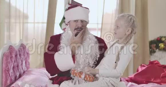 奇怪的白人女孩看着她父亲穿着圣诞老人服装假胡子脱了男人摸了摸他的脸爸爸视频的预览图