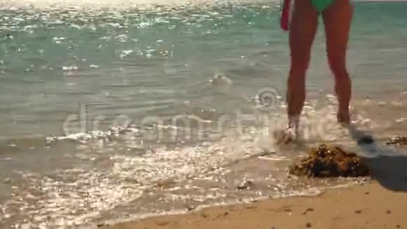 在阳光照耀的海滩上女人在浅水中散步海水冲刷着沙滩特写着她的腿视频的预览图