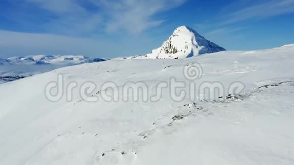 无人机在雪域上空低飞到一个人站在靠近雪车阳光明媚寒冷的一天有蓝色的滑雪板冬天的山在视频的预览图