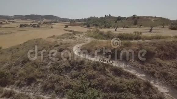 阳光明媚的一天一名男子骑着山地车在乡村风景中的空中拍摄视频的预览图
