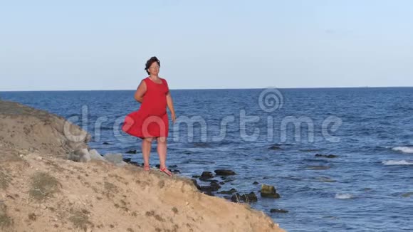 穿着红色裙子的女人在悬崖上海浪冲刷着陡峭的海岸视频的预览图