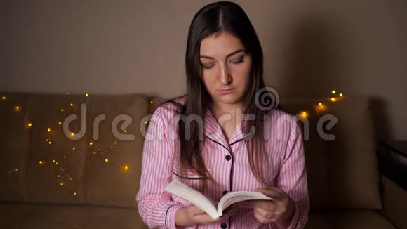 晚上一个黑发女人坐在沙发上看书轻型花环视频的预览图
