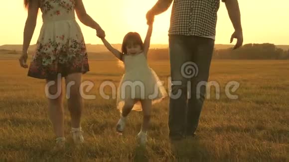 小女儿牵着爸爸妈妈的手在黄色的阳光下在公园的草地上跳跃家庭观念儿童游戏视频的预览图