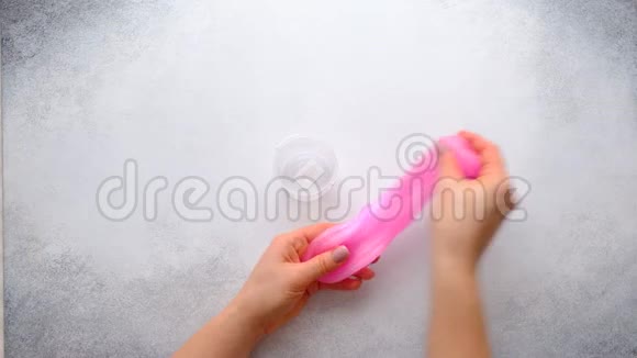 女性手在白色背景上将粉红色的黏液捣成塑料罐子时髦的液体玩具顶部视图视频的预览图