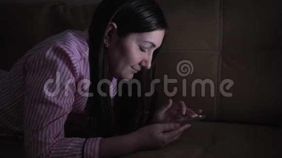 一个年轻的女人晚上在手机里浏览社交网络视频的预览图