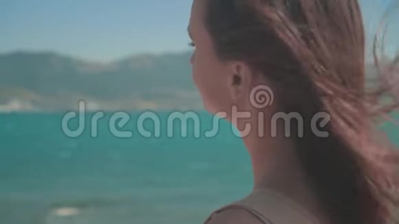 一个穿T恤的女孩长发坐在海边一个女孩坐在堤上她的头发在风中发展视频的预览图