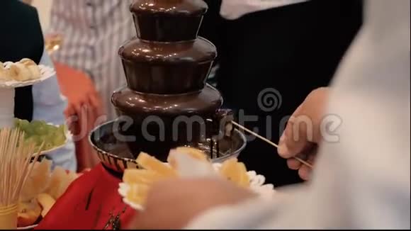 人们的手在节日的巧克力喷泉里放水果棒视频的预览图