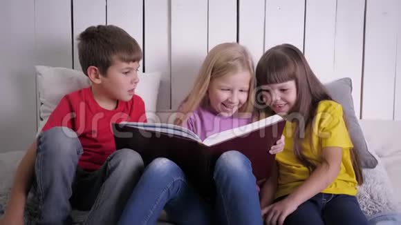在假期里穿着多色衣服的聪明孩子在家里坐在床上看书视频的预览图