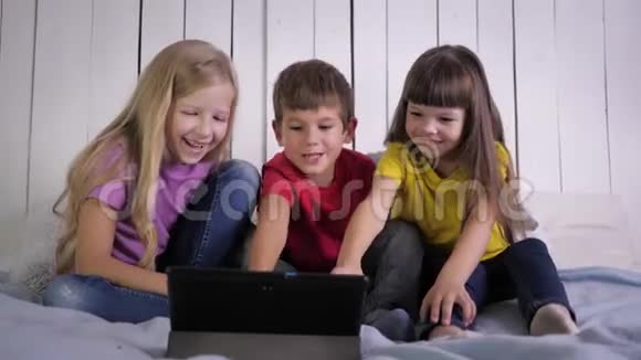 微笑的孩子们在家里放松的时候坐在床上看着数码平板电脑上的有趣视频视频的预览图