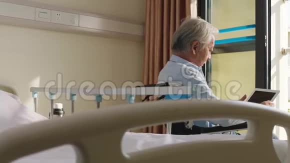 戴着数码平板电脑坐在轮椅上的亚洲老人视频的预览图