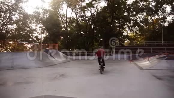 穿着红色T恤和黑色运动裤的酷bmx自行车手在美丽的夏日里做360度旋转魔术视频的预览图
