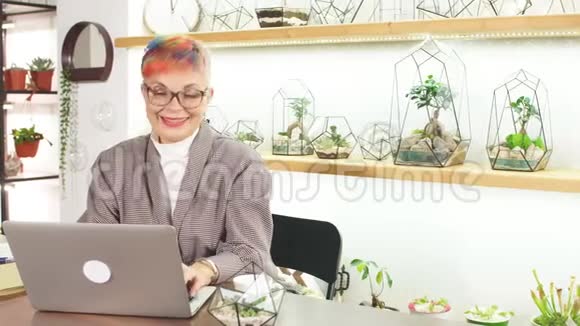 成熟的现代商务女士看着笔记本电脑屏幕微笑着打字给同事视频的预览图