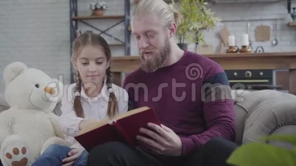 可爱的白种人女孩在书中展示了一些东西摇着头不年轻的父亲在家为女儿读书好的视频的预览图