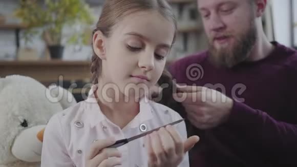一张体贴的白种人女孩留着指甲的特写脸就像微笑的父亲在后台编织她的辫子一样视频的预览图