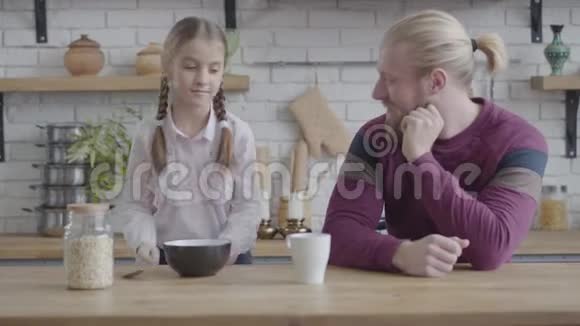 一幅美丽的白种人少女的肖像给父亲盘子和勺子用玉米片打开瓶子女儿视频的预览图
