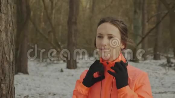 女人戴上耳机有魅力的年轻女性在户外训练前戴上耳机橙色雅克的职业运动员视频的预览图