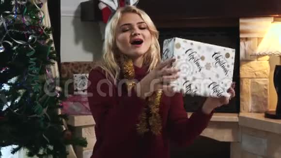 快乐的白种人金发女人抓圣诞礼物和摇动盒子的肖像微笑的年轻女孩坐着视频的预览图