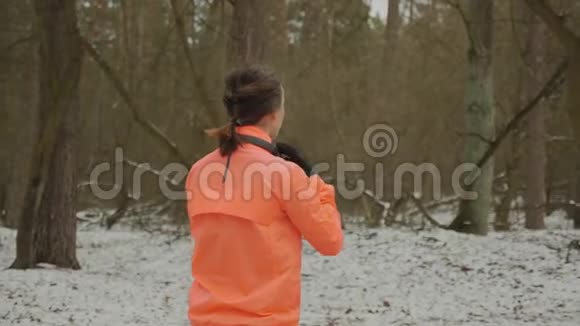 戴着耳机的女性开始在公园慢跑穿着橙色夹克的女人美丽的身体在冬天的森林里奔跑女孩在做运动视频的预览图