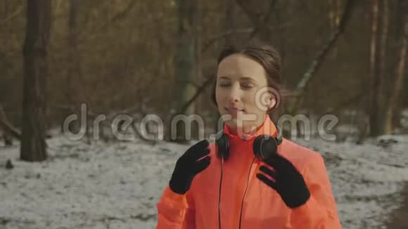 女人戴上耳机可爱的微笑女性在跑步前在公园里戴上耳机职业运动员准备艰苦的比赛视频的预览图
