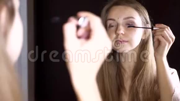 美丽的微笑女孩把睫毛膏涂在睫毛上看着镜子视频的预览图