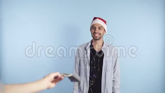 震惊的人收到纸币美元钞票一边数钱一边站在蓝墙上戴着圣诞帽视频的预览图