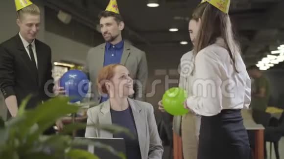 一群戴着派对帽的白种人同事围着女同事站在那里聊天愉快的中间视频的预览图