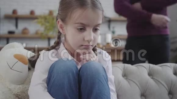 可爱的白种人黑发女孩的特写梳着辫子的辫子坐在沙发上抱着膝盖无法辨认的父亲视频的预览图
