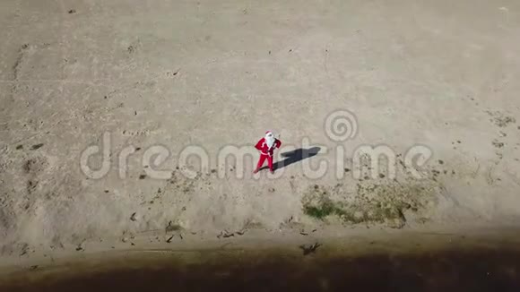 圣诞老人站在湖边的沙滩上手里拿着一个礼品袋圣诞老人挥动他的手你好相机顶级视频的预览图