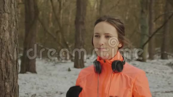 女性戴上耳机年轻的微笑女子穿着橙色夹克在跑步训练前戴上耳机做准备的性感女孩视频的预览图