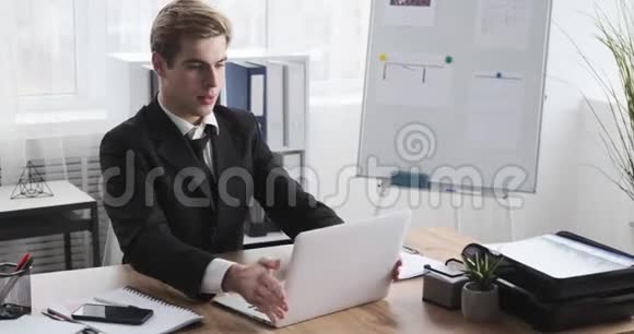 商务人员在办公室笔记本电脑上一边使用手机一边视频聊天视频的预览图