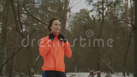 女人戴上耳机听音乐年轻微笑的女运动员在冬季公园听耳机音乐动机视频的预览图