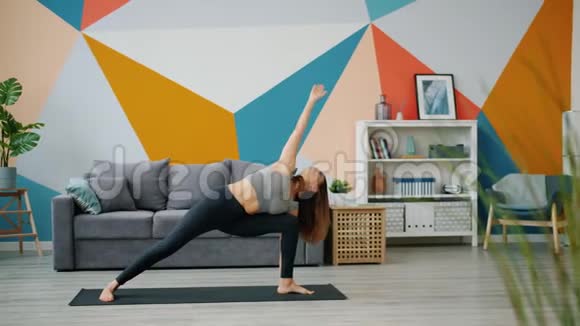 在漂亮的公寓里灵活的年轻女士在家里练习瑜伽视频的预览图