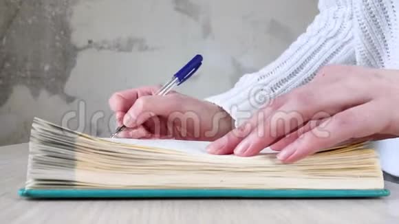 穿白色毛衣的女人写日记打开躺在桌子上的蓝色笔记本侧射特写业务规划时间管理视频的预览图