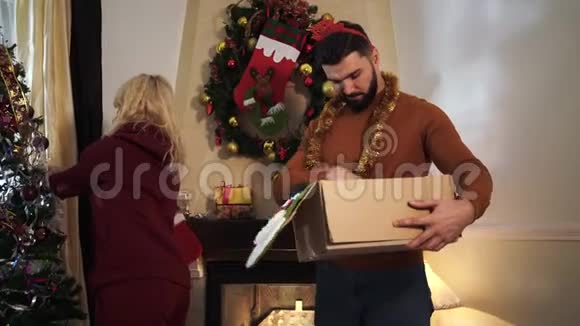 金发白种人妇女装饰圣诞树如胡须男子选择花环在盒子里年轻夫妇周末视频的预览图