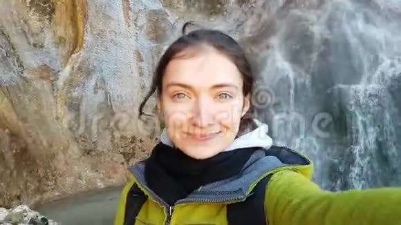 美丽微笑的黑发女孩在山和瀑布的背景上自拍风中的头发美丽的蓝眼睛视频的预览图