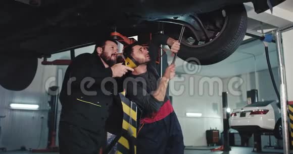 在一个现代化的汽车服务中心里两个穿制服的机械师拿着手电筒一起固定在汽车上视频的预览图