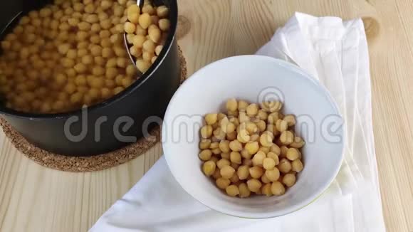 煮好的鹰嘴豆用勺子从平底锅中倒入碗中特写烹饪健康食品木桌视频的预览图