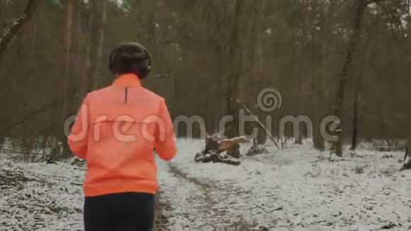 女人在公园慢跑穿着橘色夹克在冬天的森林里奔跑的的运动体的女性专业亚军准备视频的预览图