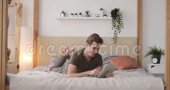 满意的男人在家里的床上使用数码平板电脑视频的预览图