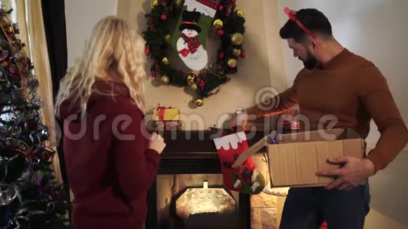 年轻的白种人夫妻用圣诞花环在墙上换新袜子正面夫妇视频的预览图