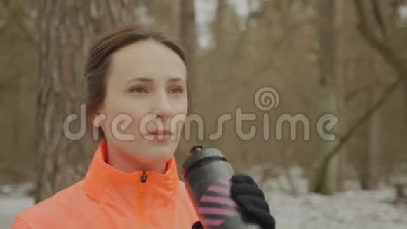 女人从瓶子里喝水年轻迷人的运动女性在冬季公园跑步训练后饮用等渗酒职业视频的预览图