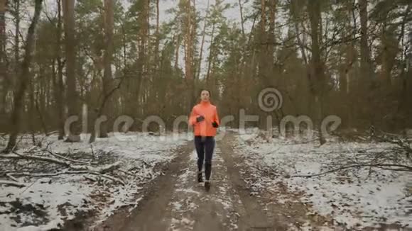 活跃的女人在冬季公园跑步早上慢跑运动服装中年轻有魅力的女运动员的正面景色视频的预览图