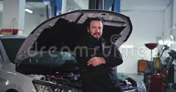 现代汽车服务中有魅力的成熟男子机械师在修理汽车时工作得很愉快听得很好视频的预览图