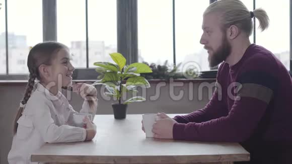 积极的白种人十几岁的女孩辫子辫子坐在桌子上与父亲和有趣的摇头快乐视频的预览图
