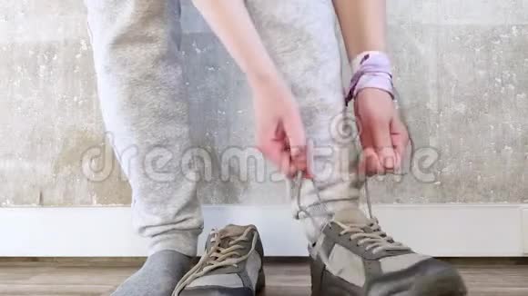 白人女孩穿着灰色裤子站在地板上穿上运动鞋系鞋带健身用运动鞋混凝土墙面视频的预览图