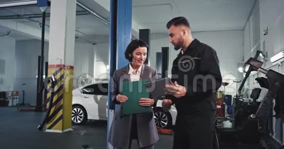 漂亮的机械师和汽车的主人或顾客很棒的女士在车库里检查发动机视频的预览图