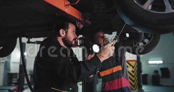 有魅力的成熟男子机械师和他的帮助在一个现代汽车服务下损坏的汽车使用手电筒视频的预览图